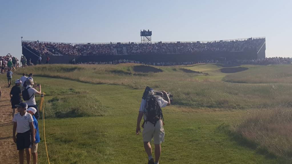 A crowd gather in a grandstand at The Open