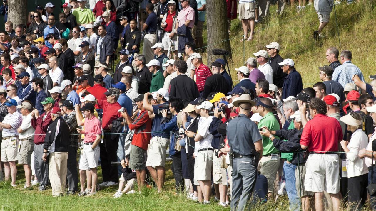 A gallery gathers behind the ropes to watch a golf event