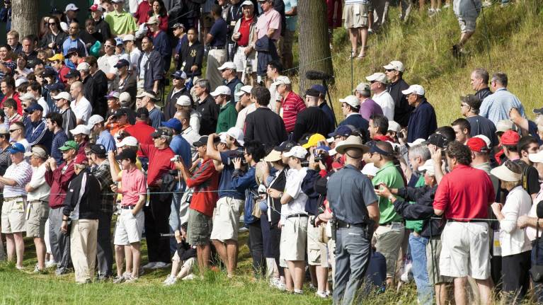A gallery watches a golf event from behind the ropes